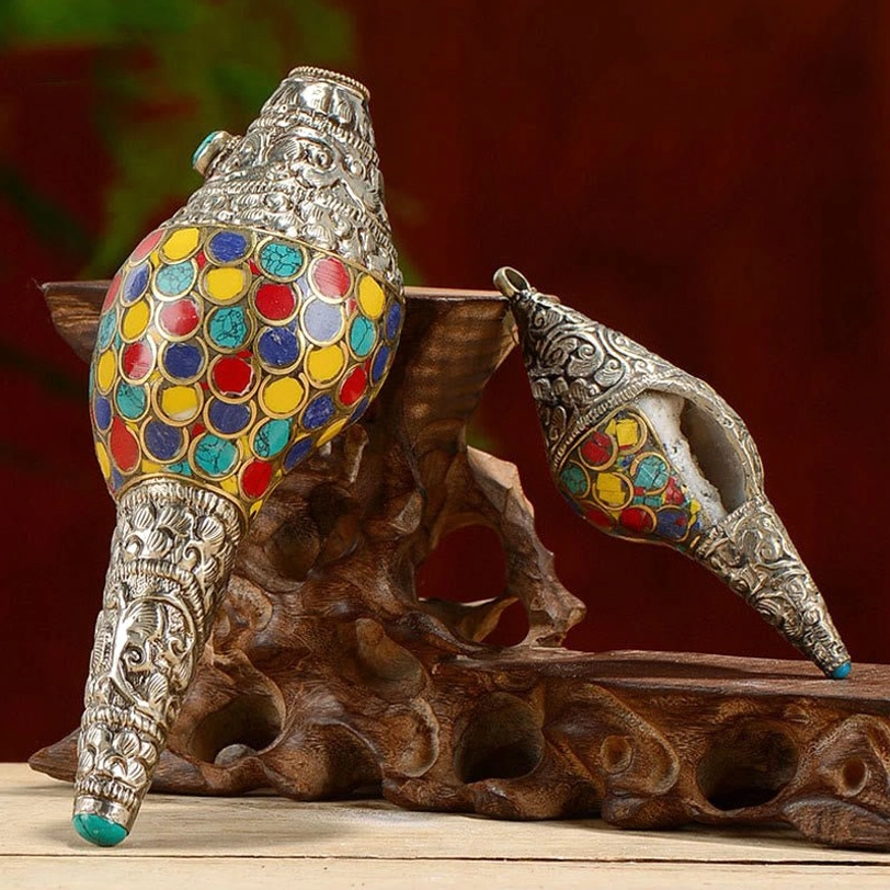 Tibetan handcrafted shankha conch shell with colorful inlays on wooden display stand and dark red backdrop