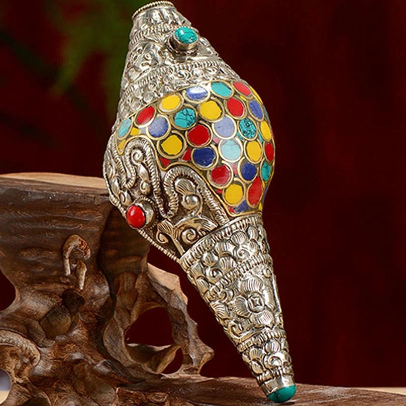 Tibetan shankha conch shell with red and turquoise gemstone inlays and intricate scroll patterns on wooden stand