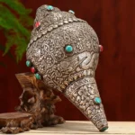 Tibetan hand-carved shankha conch shell with turquoise and coral inlays, frontal left oblique view showing engraved eight auspicious symbols and sterling silver details