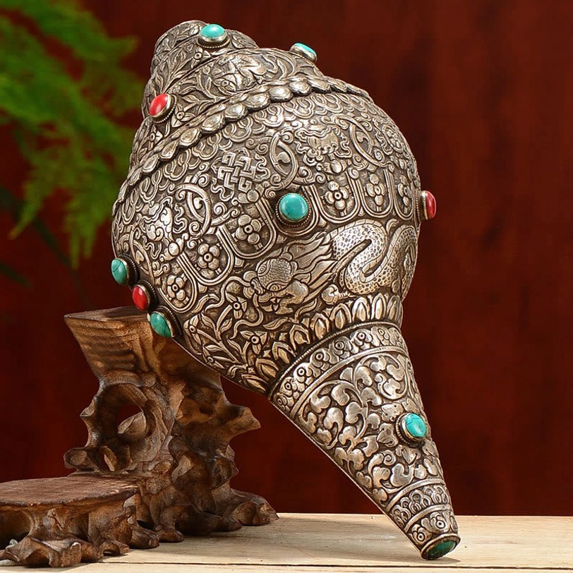 Tibetan hand-carved shankha conch shell with turquoise and coral inlays, frontal left oblique view showing engraved eight auspicious symbols and sterling silver details