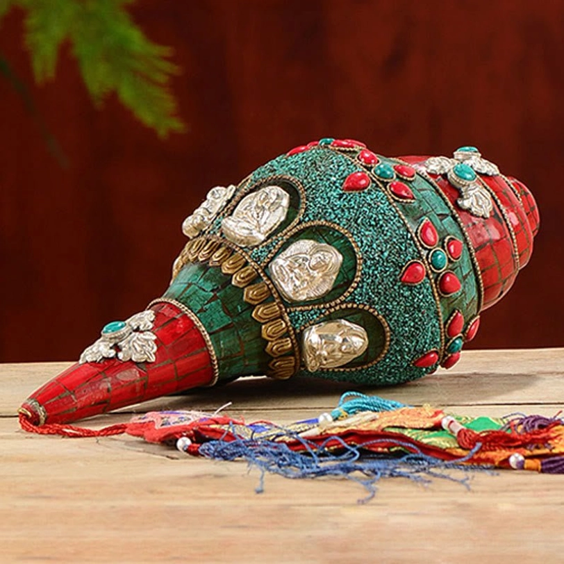 Tibetan handcrafted Shankha conch ornament with Buddha reliefs and gemstone details on wooden table