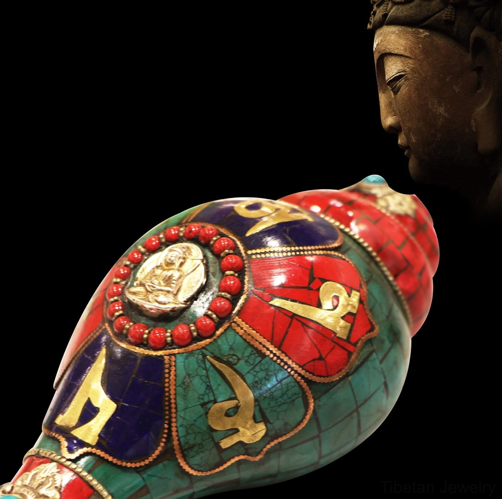Close-up overhead view of Tibetan conch shell with bronze Buddha profile and red turquoise gemstone accents