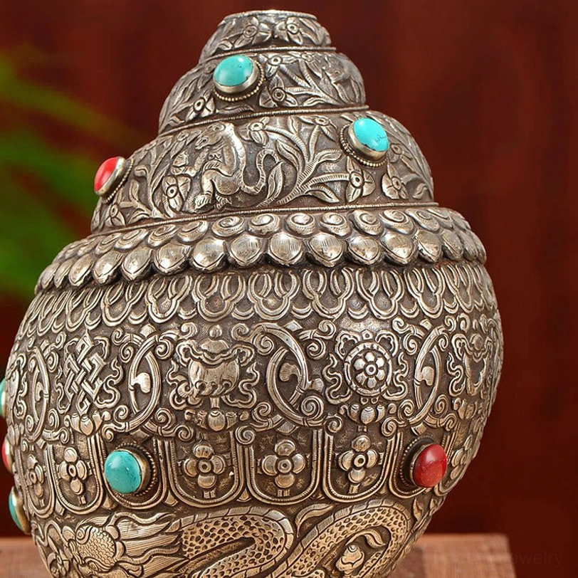 Top-down oblique view of Tibetan shankha conch shell displaying petal-shaped decorative border and complex sacred engravings with turquoise stone settings