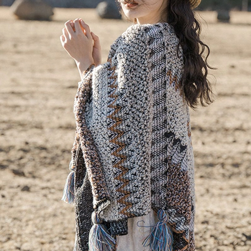 Back view of Tibetan knit shawl showing zigzag texture and blue-gray tassel trims on grassland background