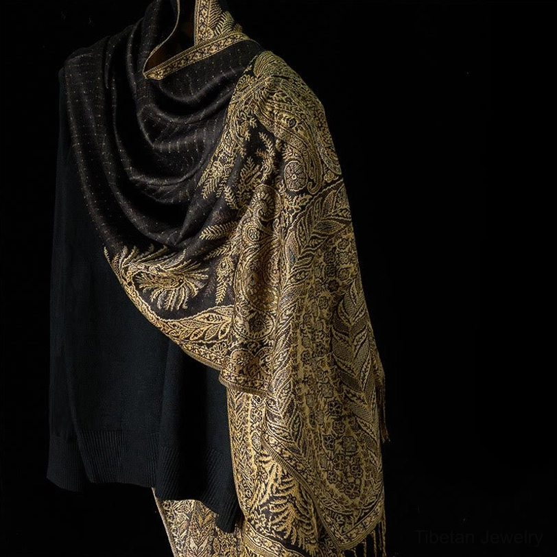 Black Tibetan shawl with ornate gold floral print and tassel hem, three-quarter side view with black knit sweater