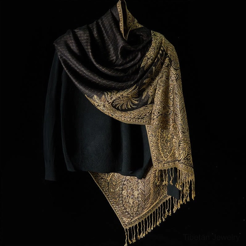 Black Tibetan paisley shawl with intricate gold patterns draped softly over dark knit sweater - front three-quarter styling