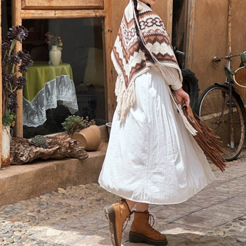 Tibetan geometric tassel shawl styled with white dress and brown boots on cobblestone street, side rear full-body view