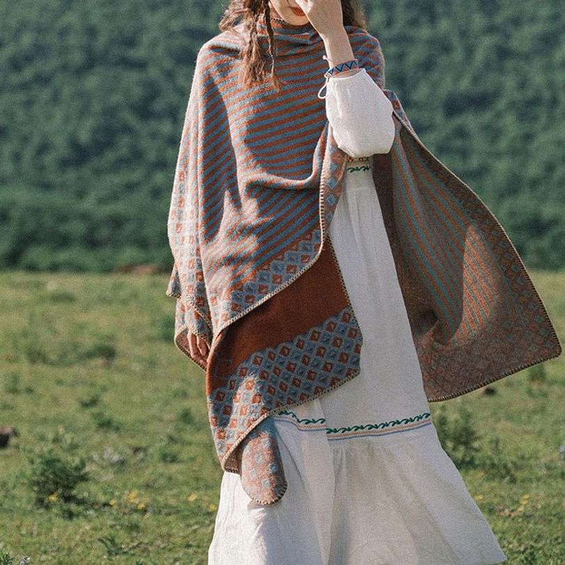 Three-quarter side view of draped Tibetan diamond shawl with asymmetric color-block hem on mountain grassland showing soft knitted texture