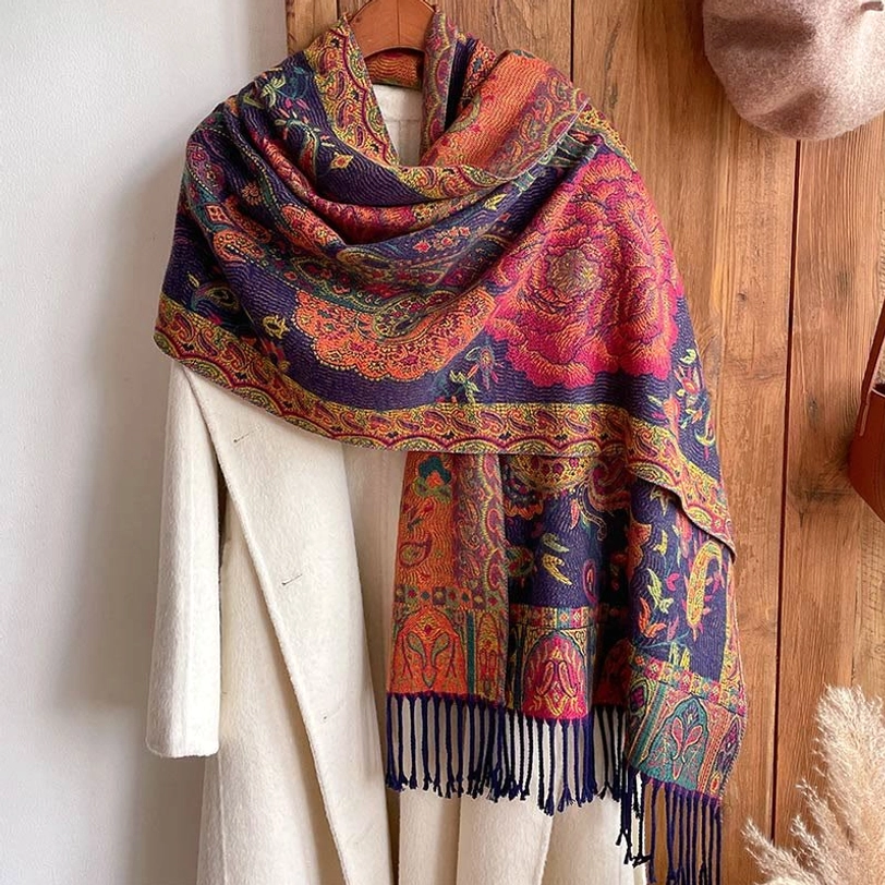Draped bohemian shawl hung over white coat on wooden wall background, full fringe edge visible, static display