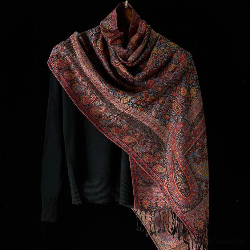Tibetan scarf laid flat display showing full paisley design, tassel hem detail, and woven texture with black styling prop