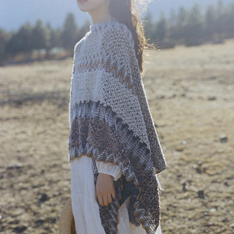 Back half-body view of Tibetan shawl displaying gradient gray-brown striped knit pattern with tassel details
