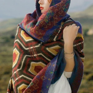 Close-up front view of woman wearing Tibetan geometric shawl with hooded drape style on alpine grassland, featuring deep red navy blue and mustard yellow colors with plush texture