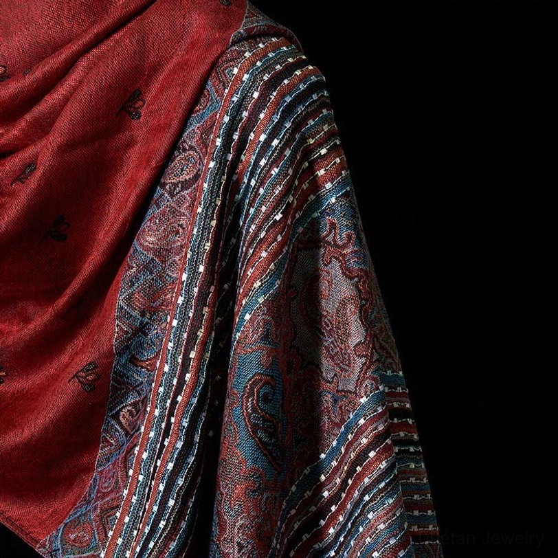 Tibetan shawl transition detail between solid red panel and woven patterned section with teal and earth tones, showcasing fabric texture and pattern combination