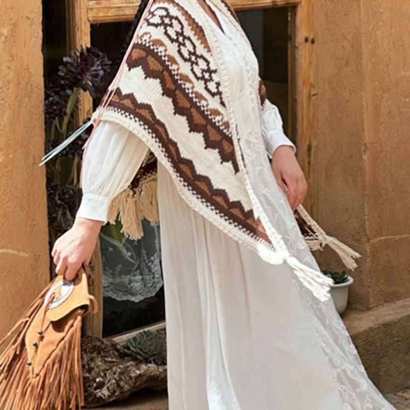 Hand holding Tibetan geometric shawl displaying tassel fringe details, side partial view at glass storefront