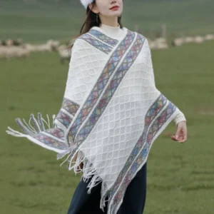 Off-white Tibetan rhombus knit tassel poncho shawl front three-quarter view on grassland with colorful ethnic border