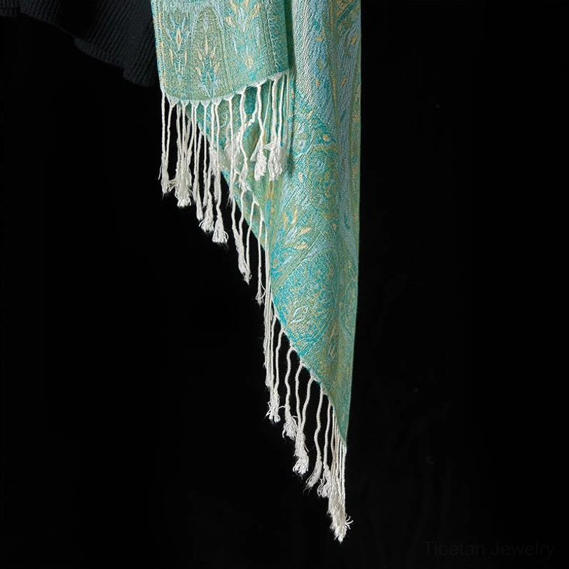 Close-up hem detail of mint green Tibetan shawl featuring long fluffy white tassel fringes on smooth woven fabric