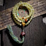 108 Tibetan sheep horn mala beads bracelet with amber guru bead, flat lay on vintage wood and Buddhist scripture background