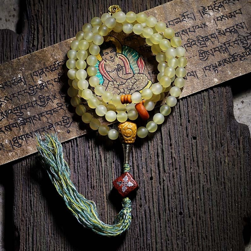 108 Tibetan sheep horn mala beads bracelet with amber guru bead, flat lay on vintage wood and Buddhist scripture background