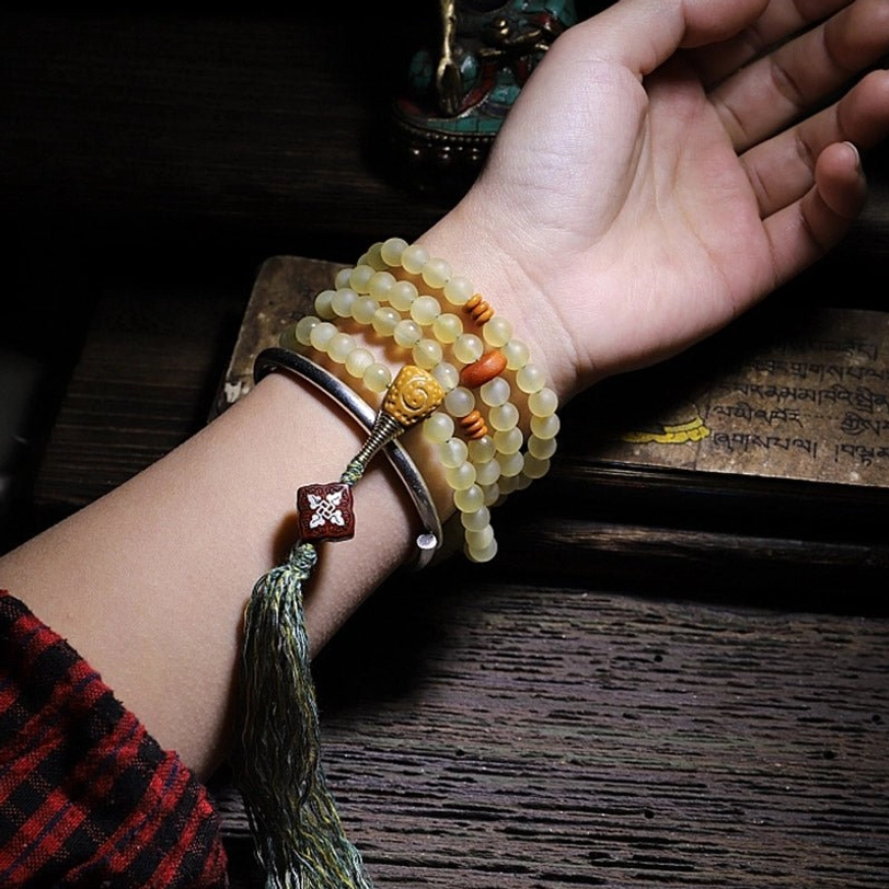 Tibetan mala bracelet worn on wrist with silver bangle, green tassel pendant on vintage wood background