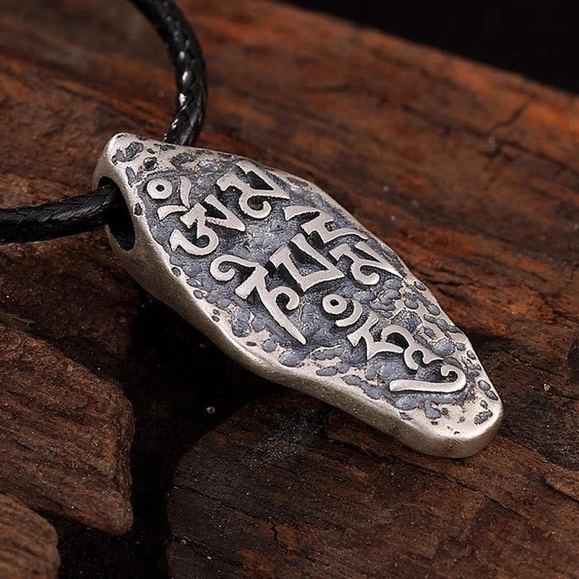 Carved Sanskrit text on Tibetan silver pendant showing aged patina and Buddhist mantra details