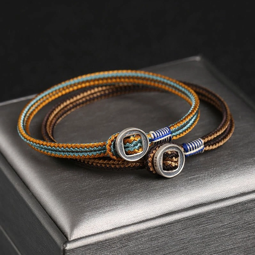 Handmade tibetan silver protection bracelet with brown and blue woven cord, silver button clasp, displayed on elegant silver jewelry box