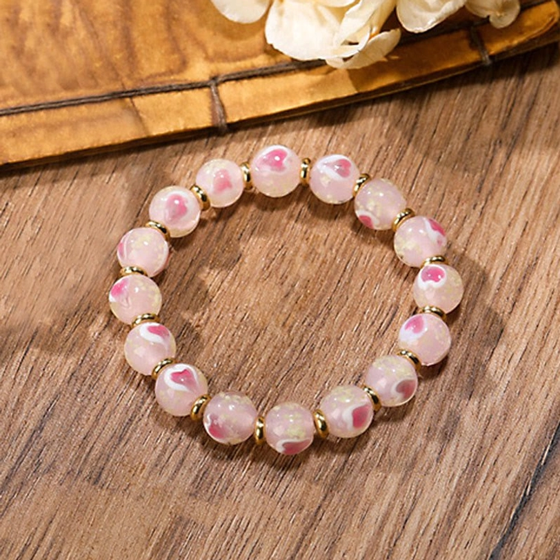 Single Tibetan simple version bracelet with luminous pink glass beads and gold spacer accents on wooden surface
