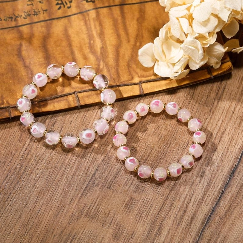 Two simple Tibetan bracelets with pink-white glass beads and small gold bead accents on wooden table