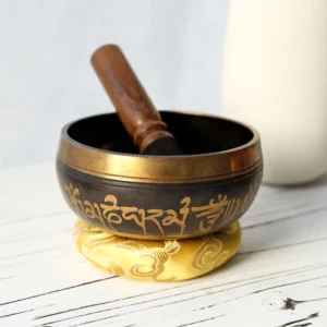 Hand-hammered Tibetan bronze singing bowl with Om Mani Padme Hum mantra engraving, displayed with embroidered cushion and wooden mallet for meditation practice