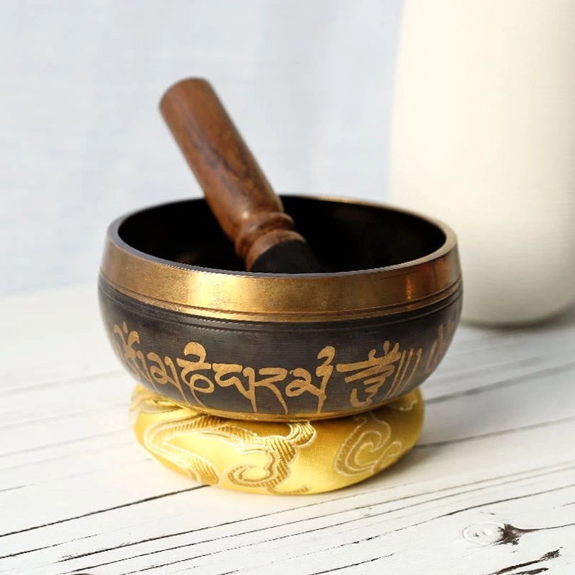 Hand-hammered Tibetan bronze singing bowl with Om Mani Padme Hum mantra engraving, displayed with embroidered cushion and wooden mallet for meditation practice