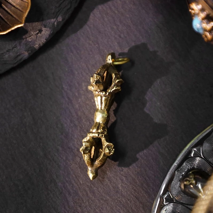 Traditional single dorje vajra pendant with aged bronze metal finish - hand-carved ritual motifs and spiritual symbolism on dark fabric background
