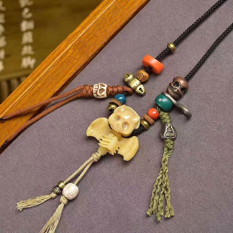 Tibetan skull bat necklace overhead view on wooden tray - showing brown braided cords with green tassel and double skull pendants