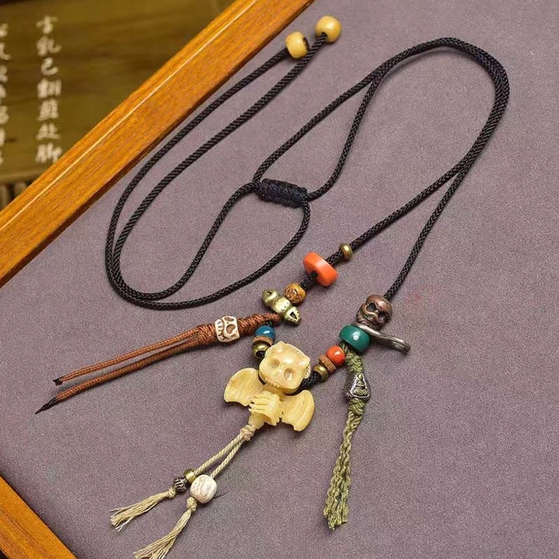 Tibetan skull bat pendant necklace variation with brown braided cord and orange blue beads - overhead angled view on wooden tray