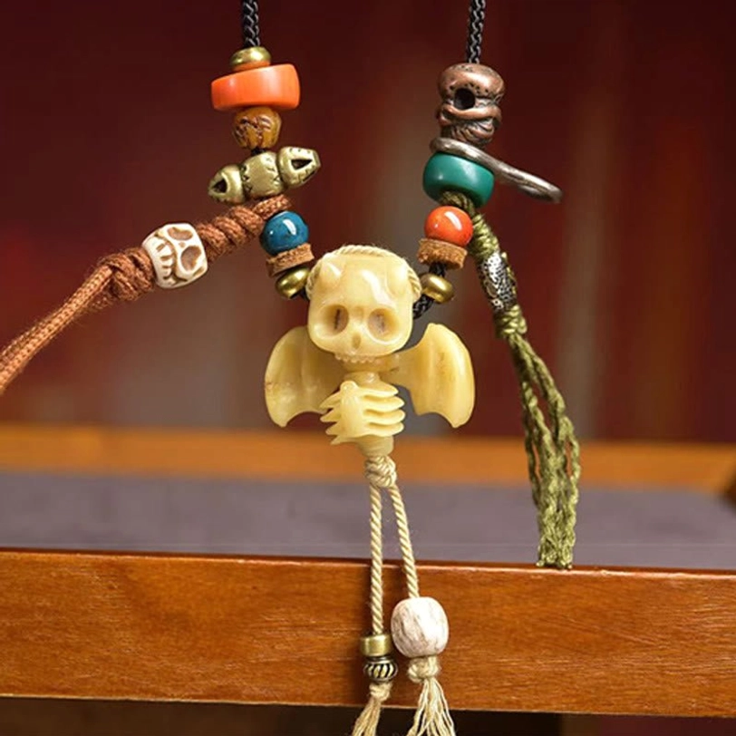 Front close-up of Tibetan skull bat necklace on wooden shelf - beige bone skull design with green red decorative beads and brass hardware