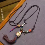 Tibetan skull bone necklace with beige skull pendant, dark brown rope cord, and multicolor tassel charm - traditional Tibetan protective amulet jewelry