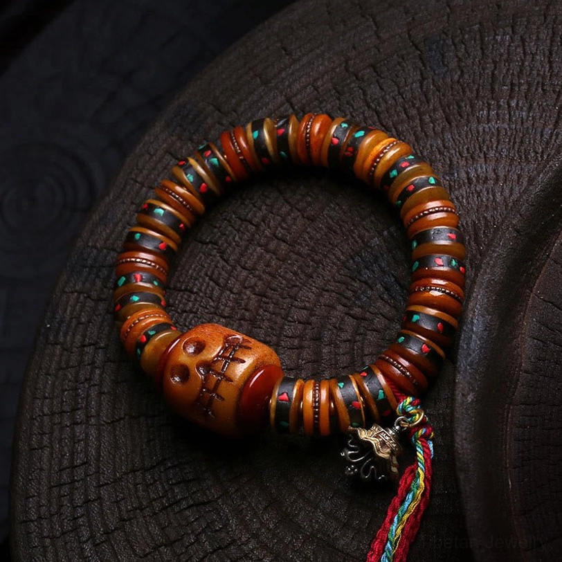 Tibetan bone skull bracelet with carved focal bead, colorful tassel, and metal charm on wooden background