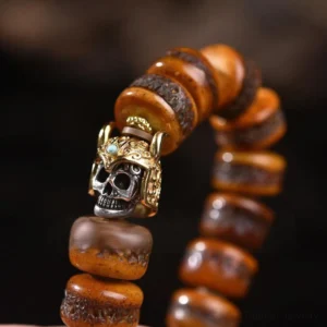 Close-up side view of bone bead bracelet with warrior-style metal skull pendant hanging in studio light