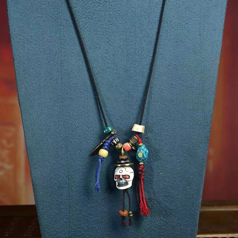 Tibetan skull necklace displayed on blue velvet background - showing double braided black cord with bone skull pendant and tassels