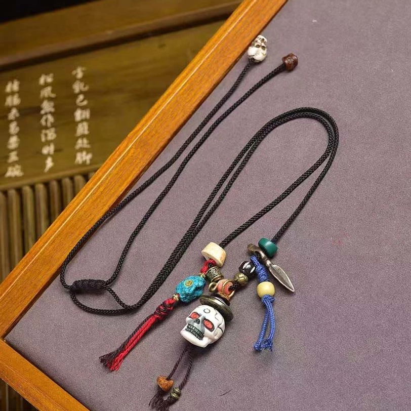 Tibetan skull Lord of Corpse Forest bone necklace pendant with braided cord and mixed agate beads - overhead angled view on wooden tray