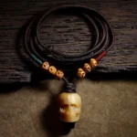 Tibetan camel bone skull pendant necklace with braided dark brown cord on rustic wooden table, overhead flat lay view