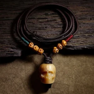 Tibetan camel bone skull pendant necklace with braided dark brown cord on rustic wooden table, overhead flat lay view