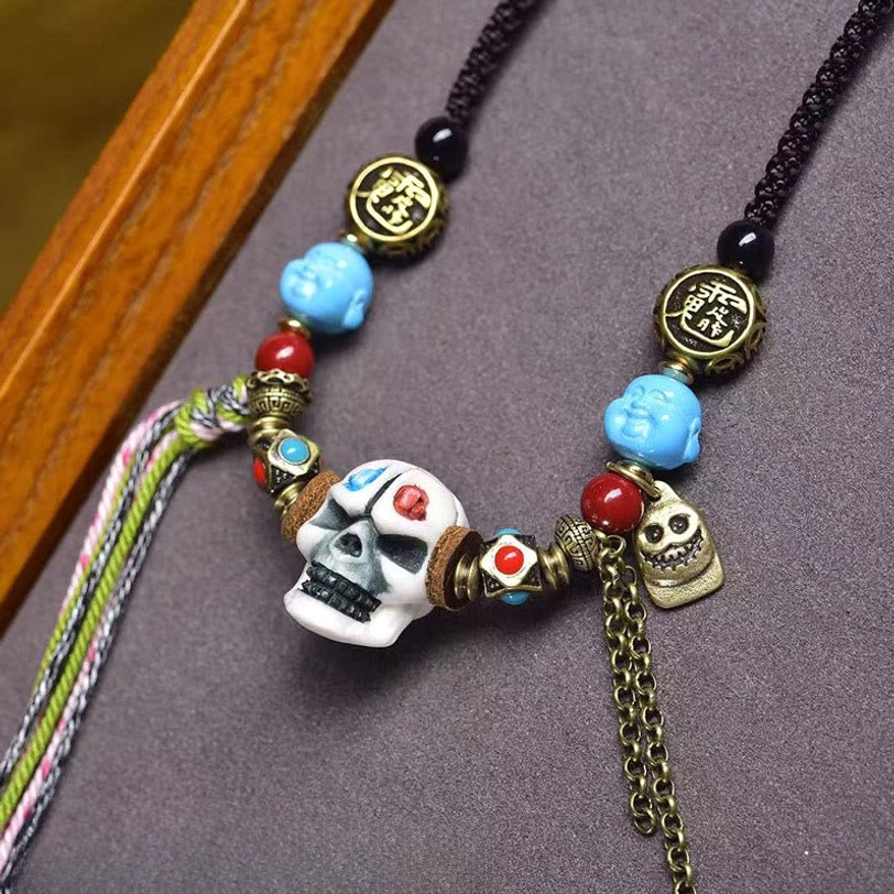 Detailed Tibetan skull necklace featuring carved blue agate beads, brass Chinese character charms, multicolor tassel, and handcrafted bone pendant