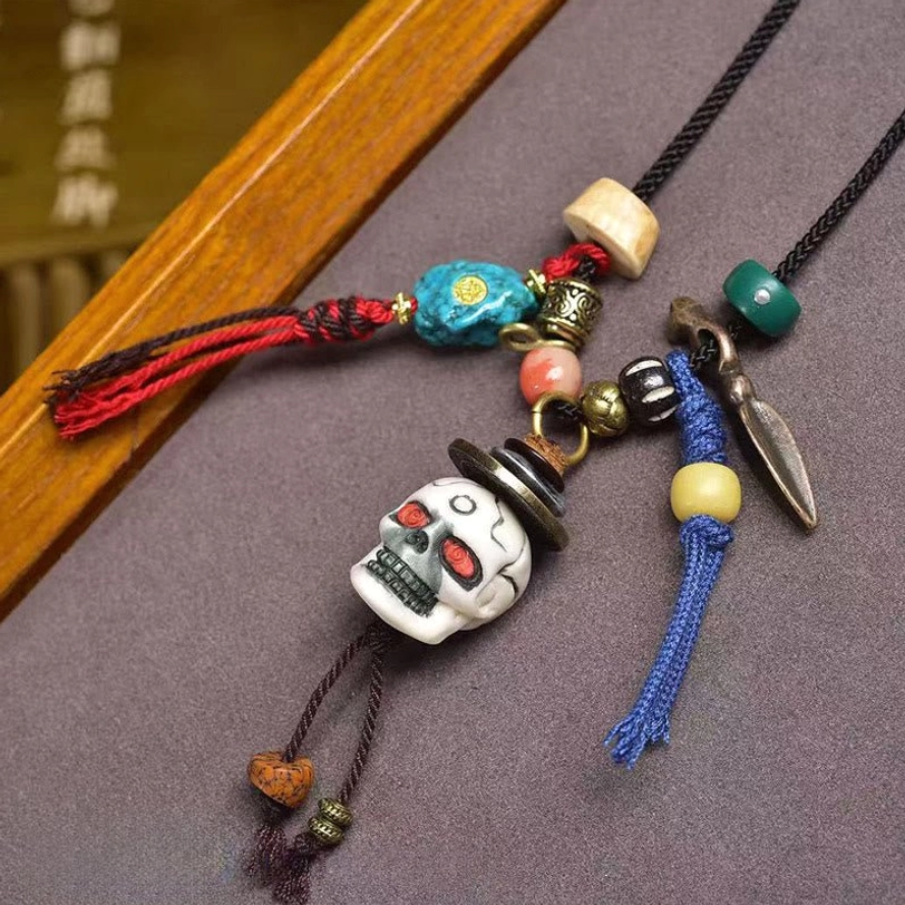 Close-up top-down view of handmade Tibetan skull necklace showing white bone skull pendant with tassel and copper metal accessories