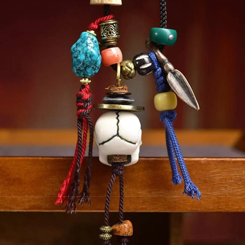 Side angle view of Tibetan skull bone necklace on wooden shelf - showing skull charm with blue tassel and copper hardware