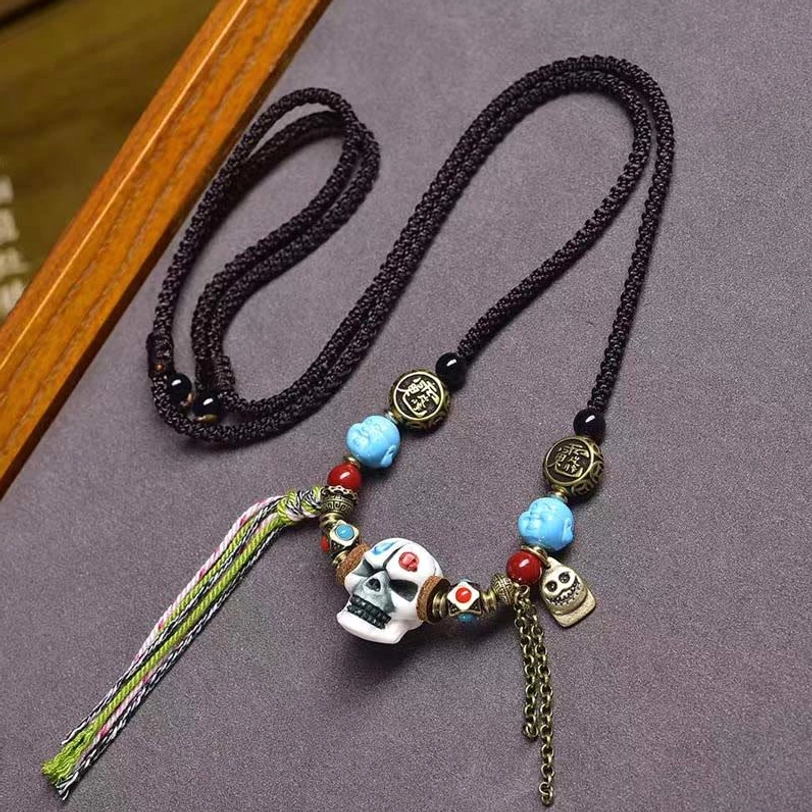 Tibetan protective skull bone necklace with white skull pendant, black woven cord, blue and red healing gemstone beads, and metal chain charm