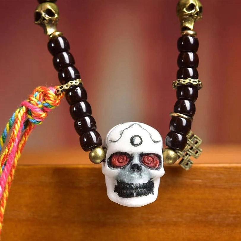 Close-up of carved white skull pendant with red eyes and colorful tassel, brass metal accents