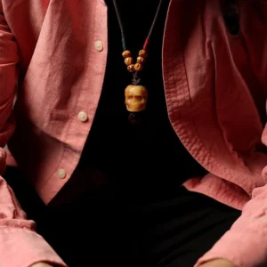 Hand-carved bone skull pendant worn on dark braided cord, styled on pink fabric, Tibetan protection necklace worn view