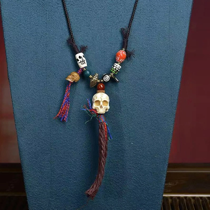 Tibetan protective skull amulet necklace with black cord, tiny skull bone beads, brown tassel, and spiritual design on dark blue fabric background