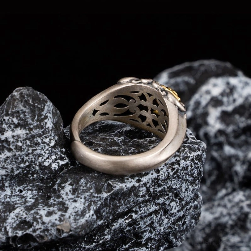 Frontal flat view of vintage-style Tibetan protective skull ring with embossed gold front and carved silver edges on dark wood background