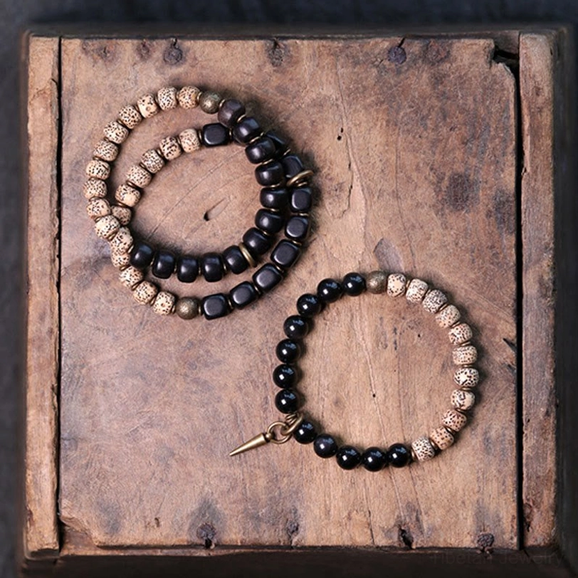 Three Tibetan Bodhi Seed bracelets arranged in wooden tray with spike metal charms and black stone beads