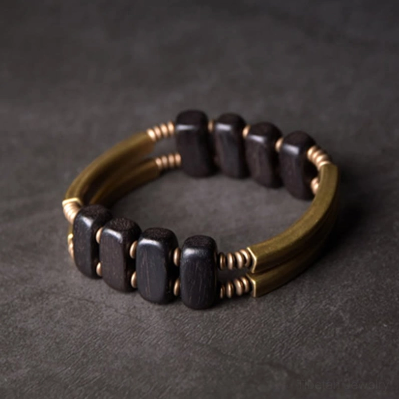 Square ebony bead double layer tibetan brass bracelet direct top-down view on dark grey concrete background, displaying square dark ebony beads with curved gold brass bars in circular loop